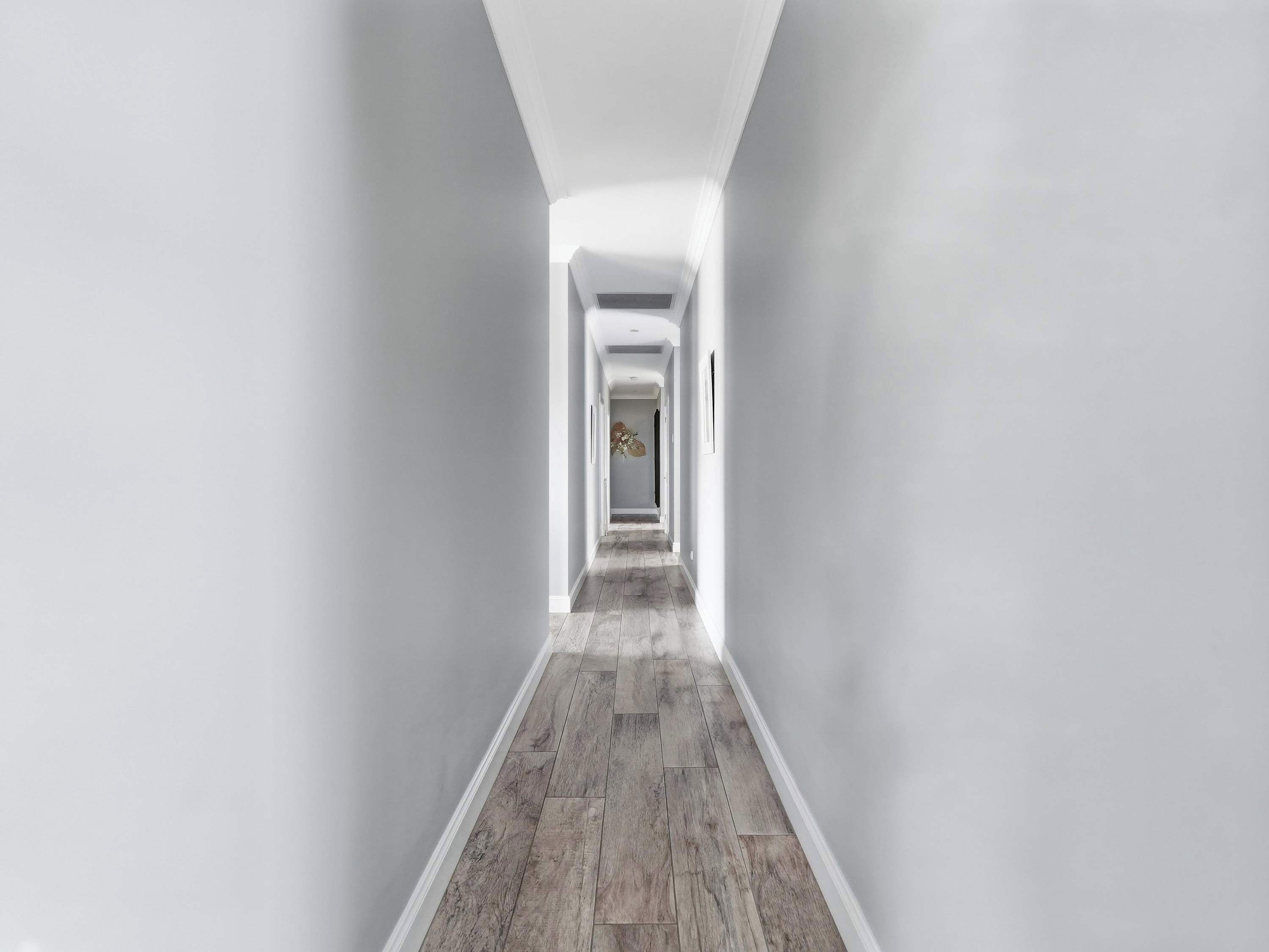 A narrow hallway with a wooden floor and white walls.