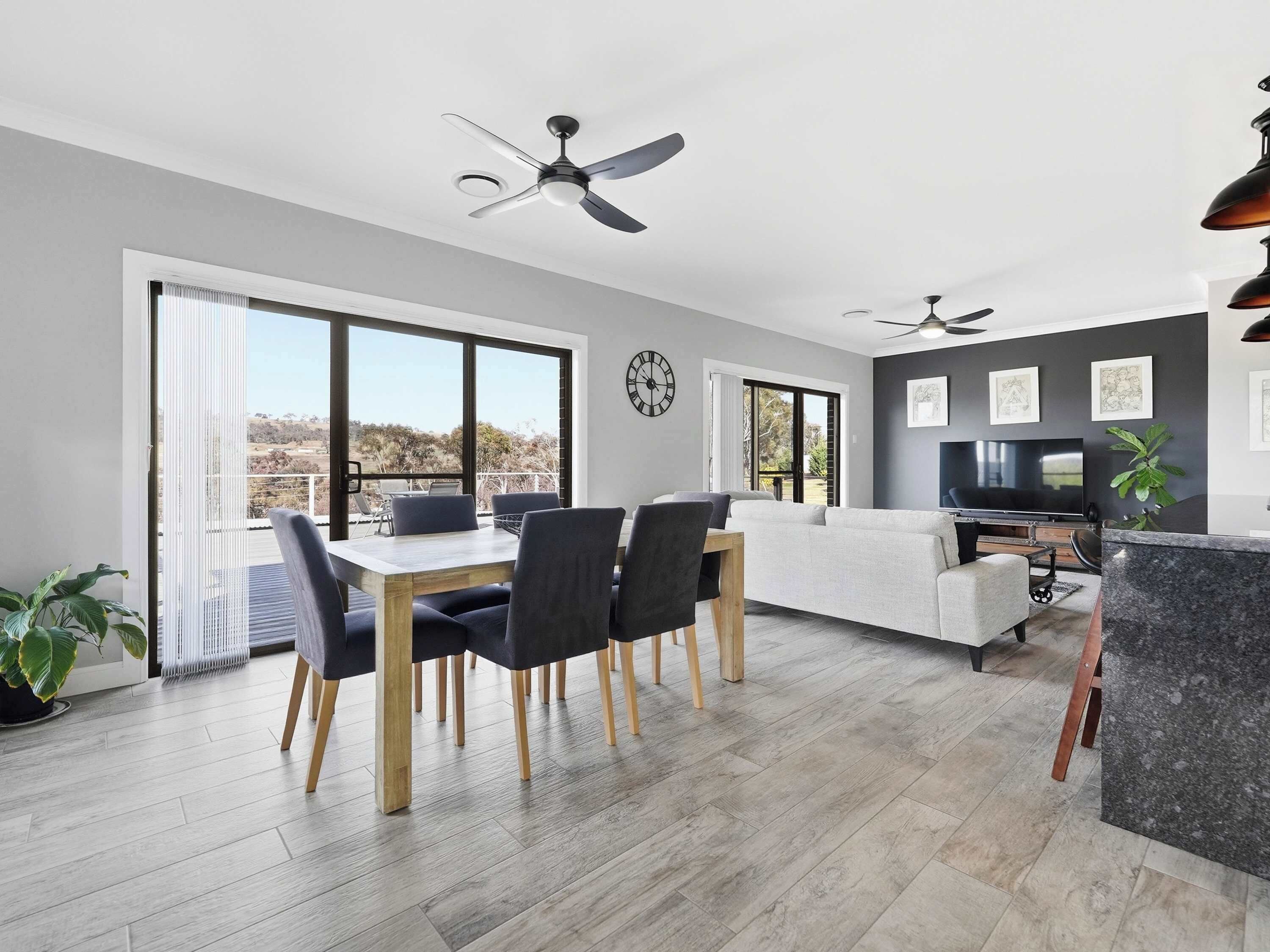 A modern living space with a dining area, sofa, TV, and large windows.