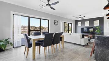 A modern living space with a dining area, sofa, TV, and large windows.