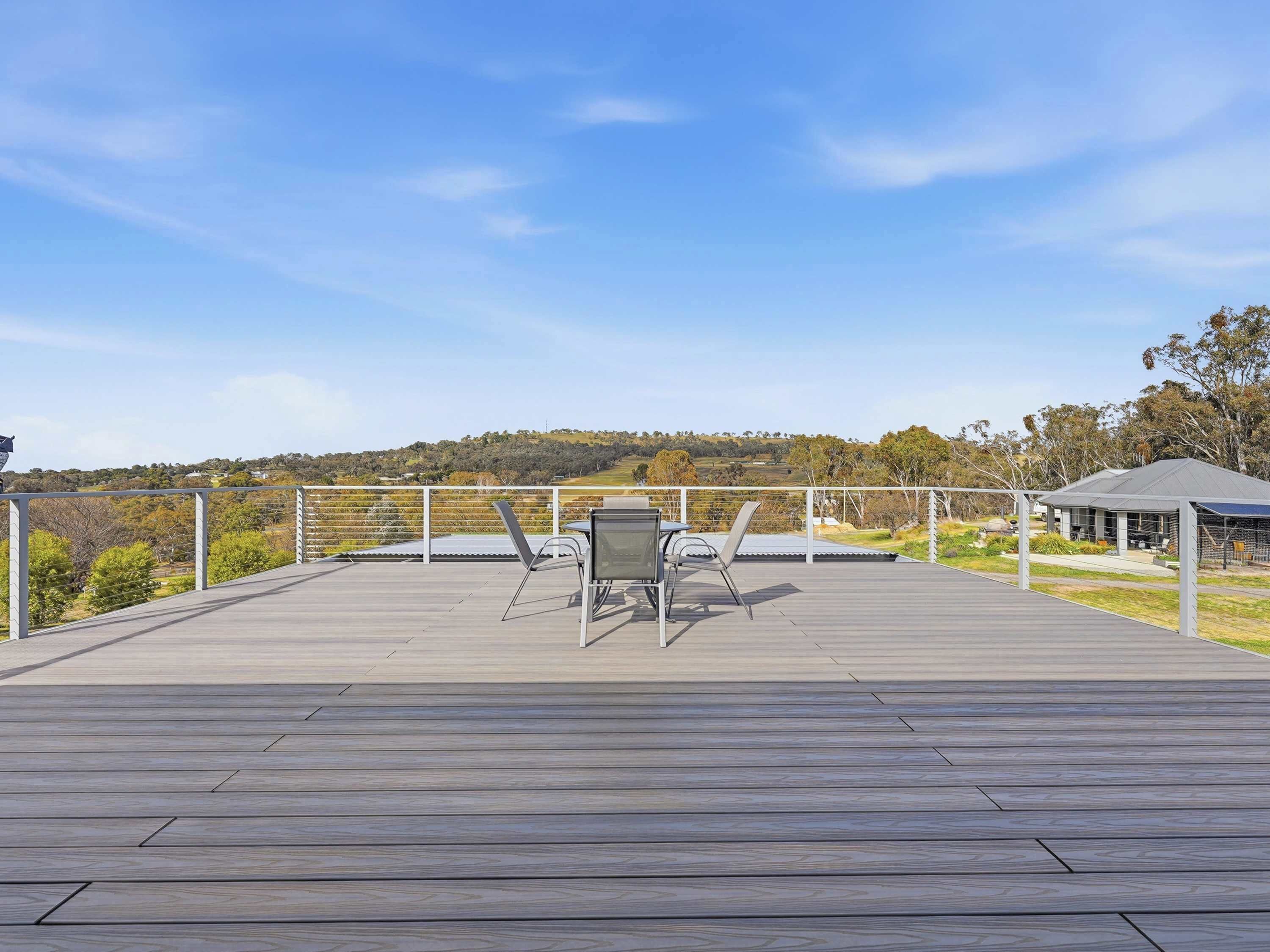 A wooden deck with a table and chairs, overlooking a hilly landscape.