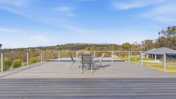 A wooden deck with a table and chairs, overlooking a hilly landscape.