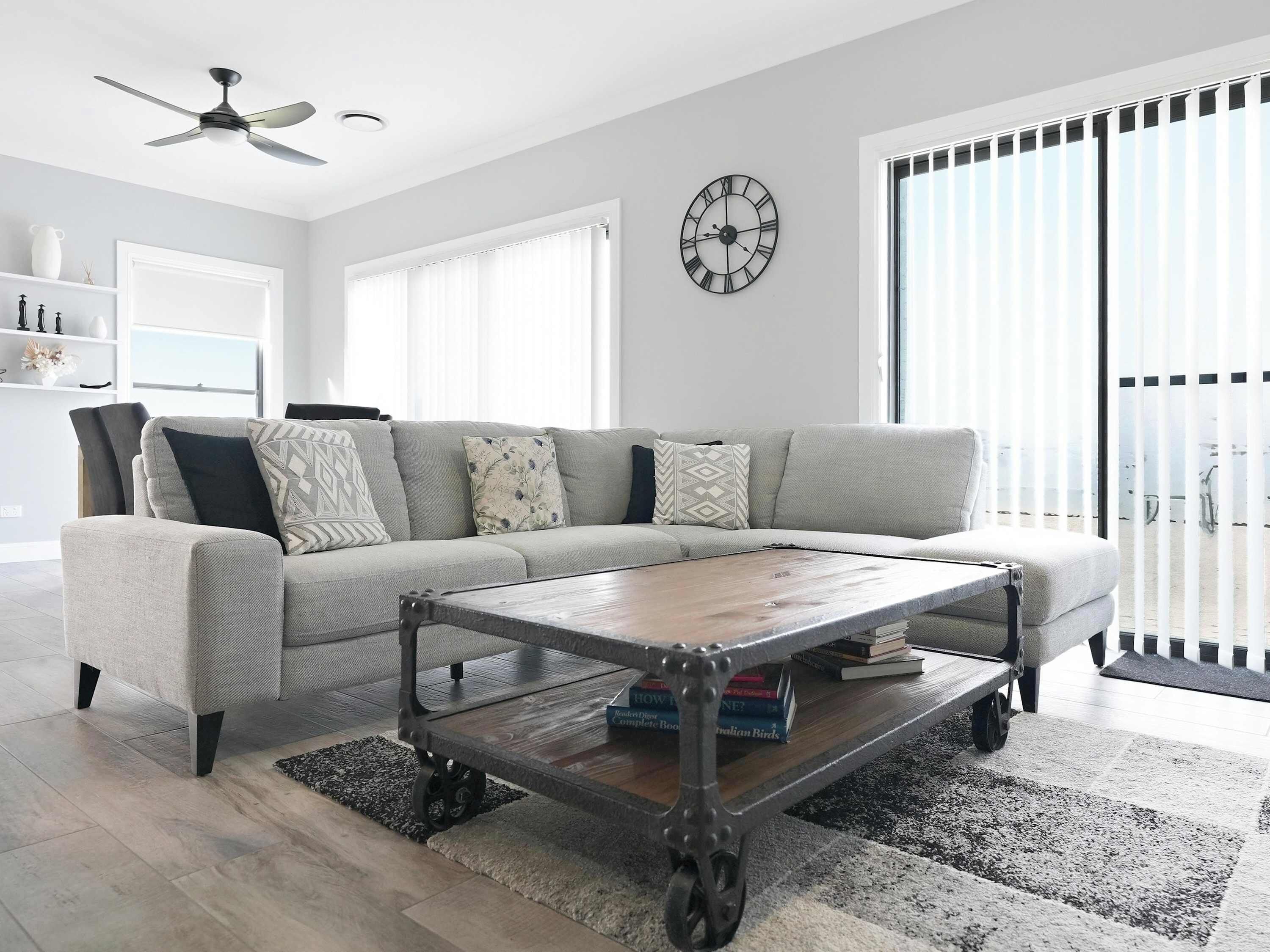Ein modernes Wohnzimmer mit einem grauen Sofa, einem Holztisch und einer großen Wanduhr.