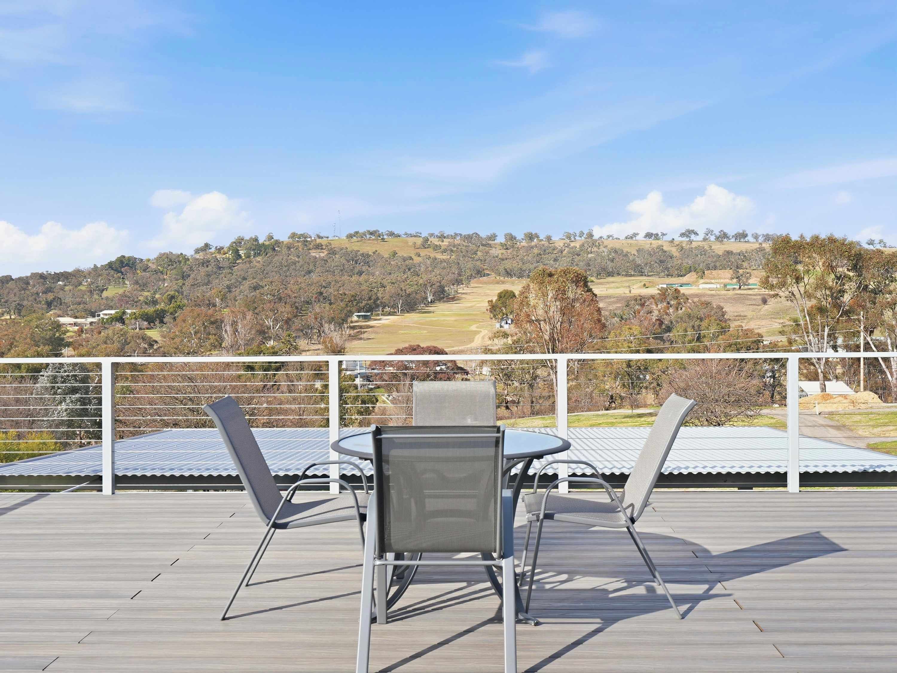 A deck with two chairs and a table, overlooking a hilly landscape with trees and buildings.