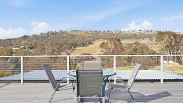 A deck with two chairs and a table, overlooking a hilly landscape with trees and buildings.