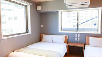 Habitación de hotel con dos camas, una ventana, un aire acondicionado y vistas a un edificio.
