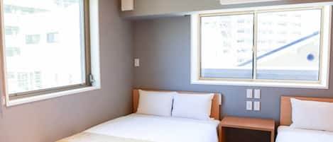 Habitación de hotel con dos camas, una ventana, un aire acondicionado y vistas a un edificio.