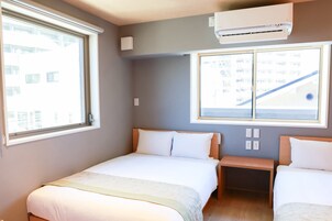 Habitación de hotel con dos camas, una ventana, un aire acondicionado y vistas a un edificio.