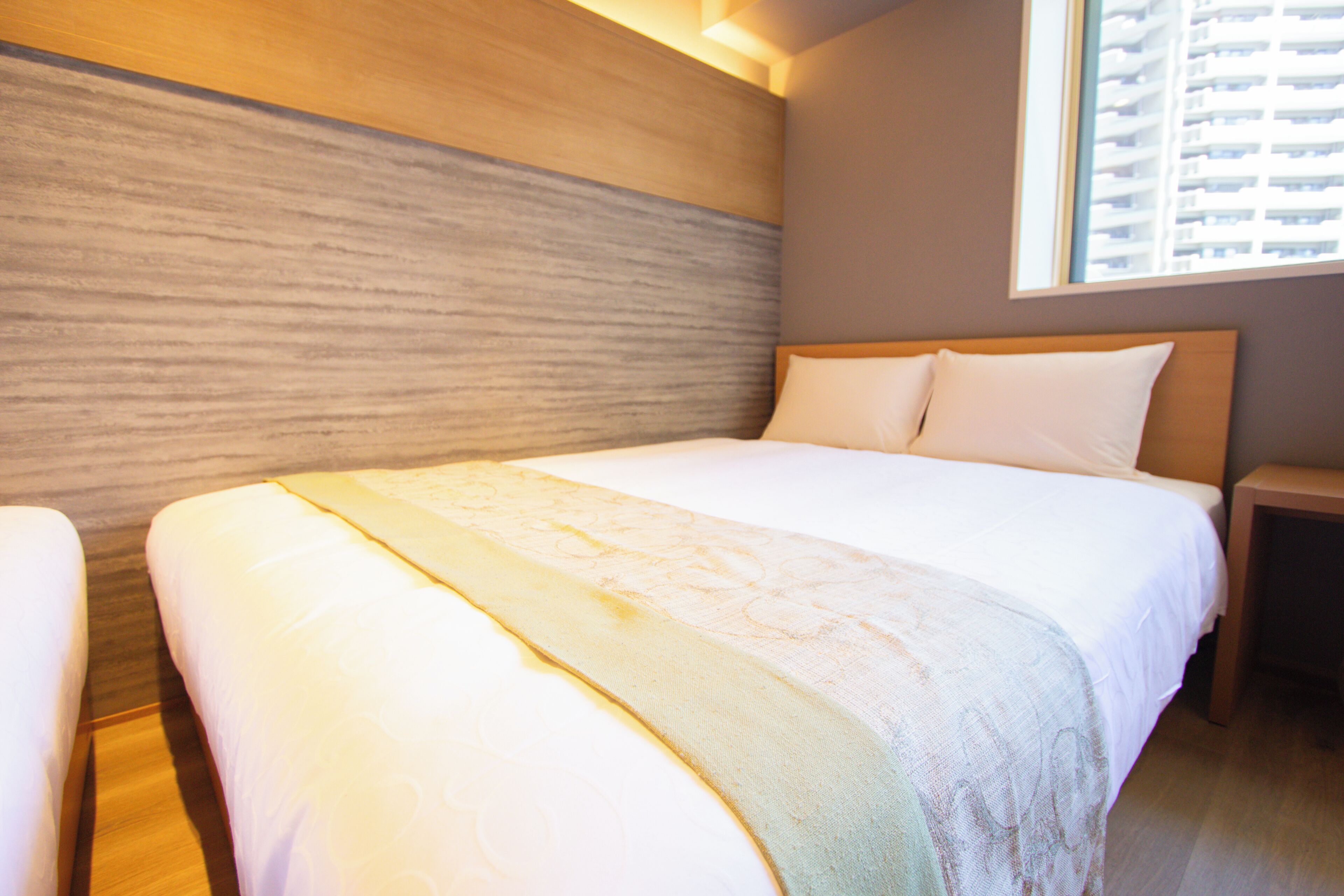A hotel room with a large bed, wooden headboard, and a window with a view of buildings.