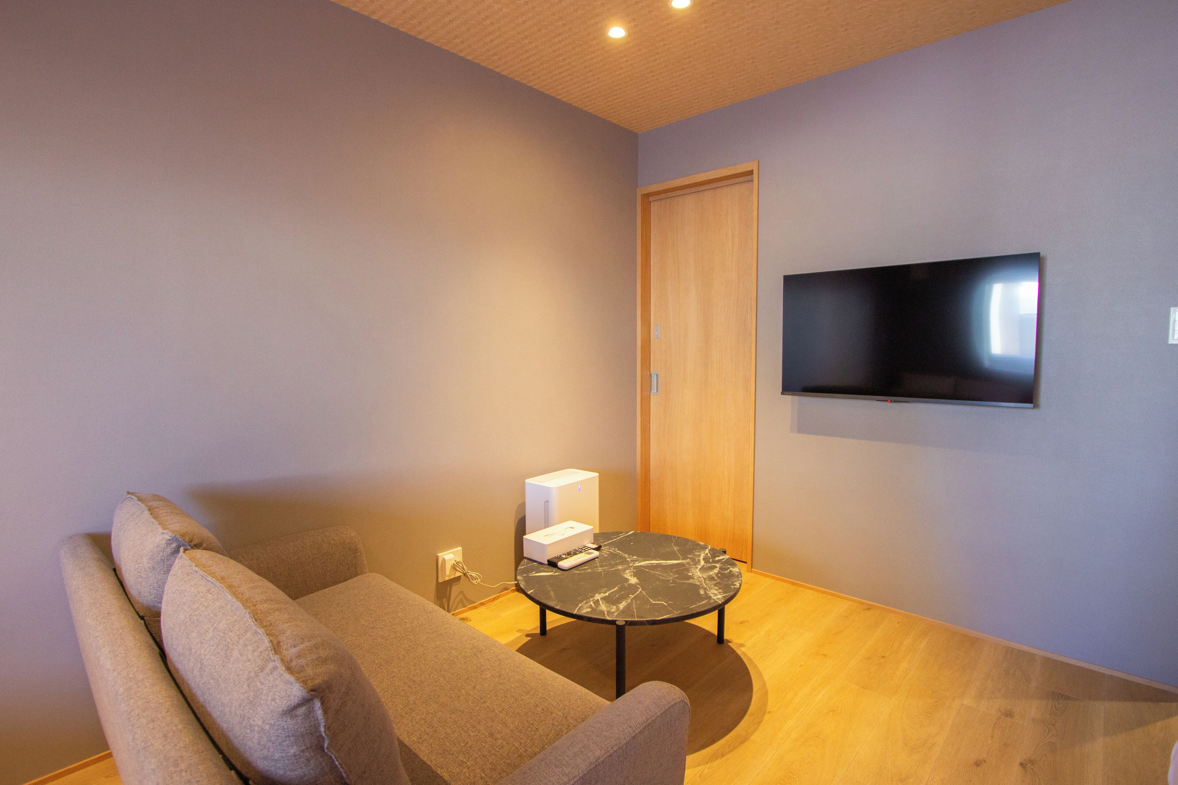 Una sala de estar moderna con una televisión de pantalla plana montada en la pared, un sofá, una mesa de centro y piso de madera.