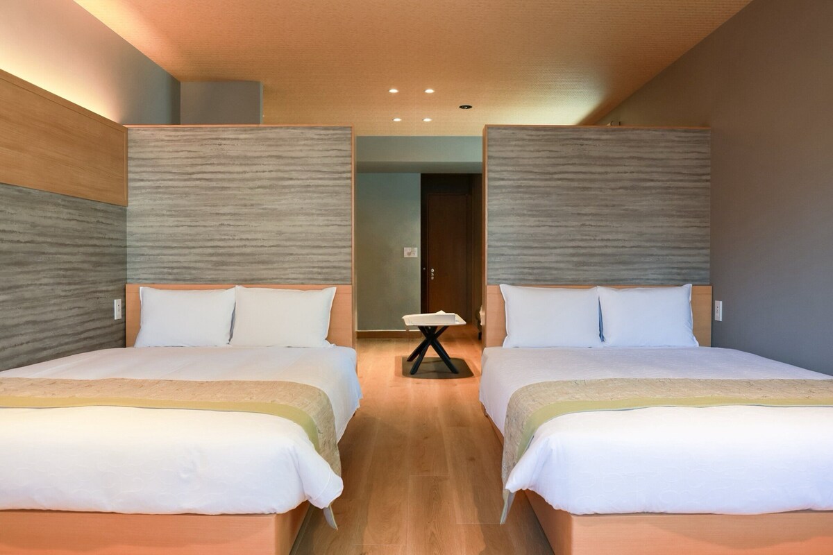 Una habitación de hotel con dos camas, una mesita y una puerta que da a otra estancia.