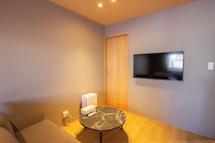 Una habitación con una televisión de pantalla plana en la pared, una pequeña mesa redonda con un control remoto y un sofá.