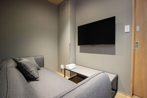 A modern hotel room with a grey sofa, a flat-screen TV mounted on the wall, and a small table with a remote control. - Nonette Hakata Haruyoshi (Fukuoka City)