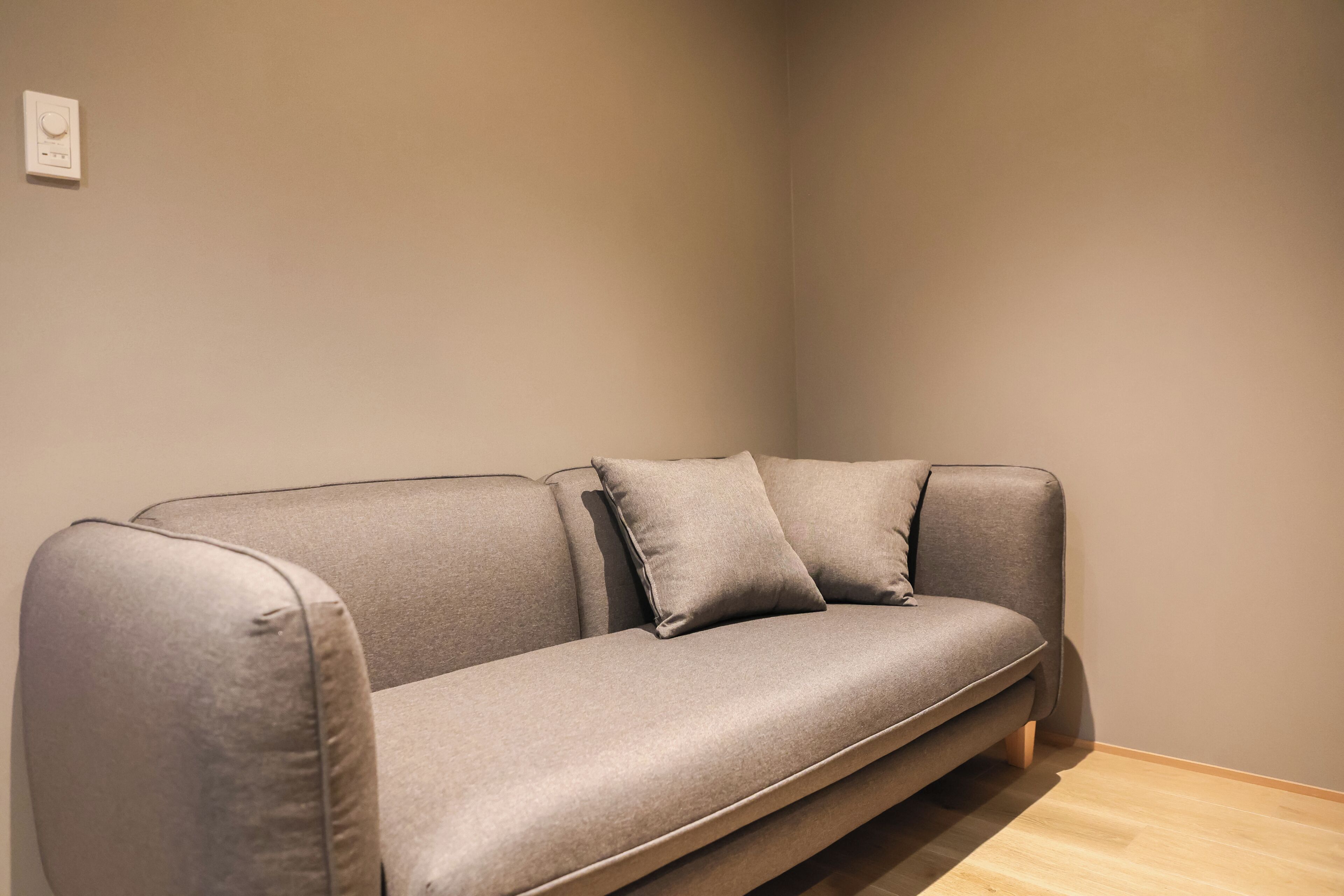 A modern grey sofa with a wooden base against a plain wall.