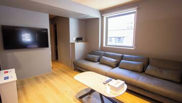 Una sala de estar moderna con un televisor de pantalla plana montado en la pared, un sofá, una mesa de centro y un ventanal que proporciona luz natural.