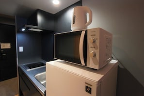 A compact kitchen with a microwave on top of a refrigerator, a sink, and a stove. - Nonette Hakata Haruyoshi (Fukuoka City)