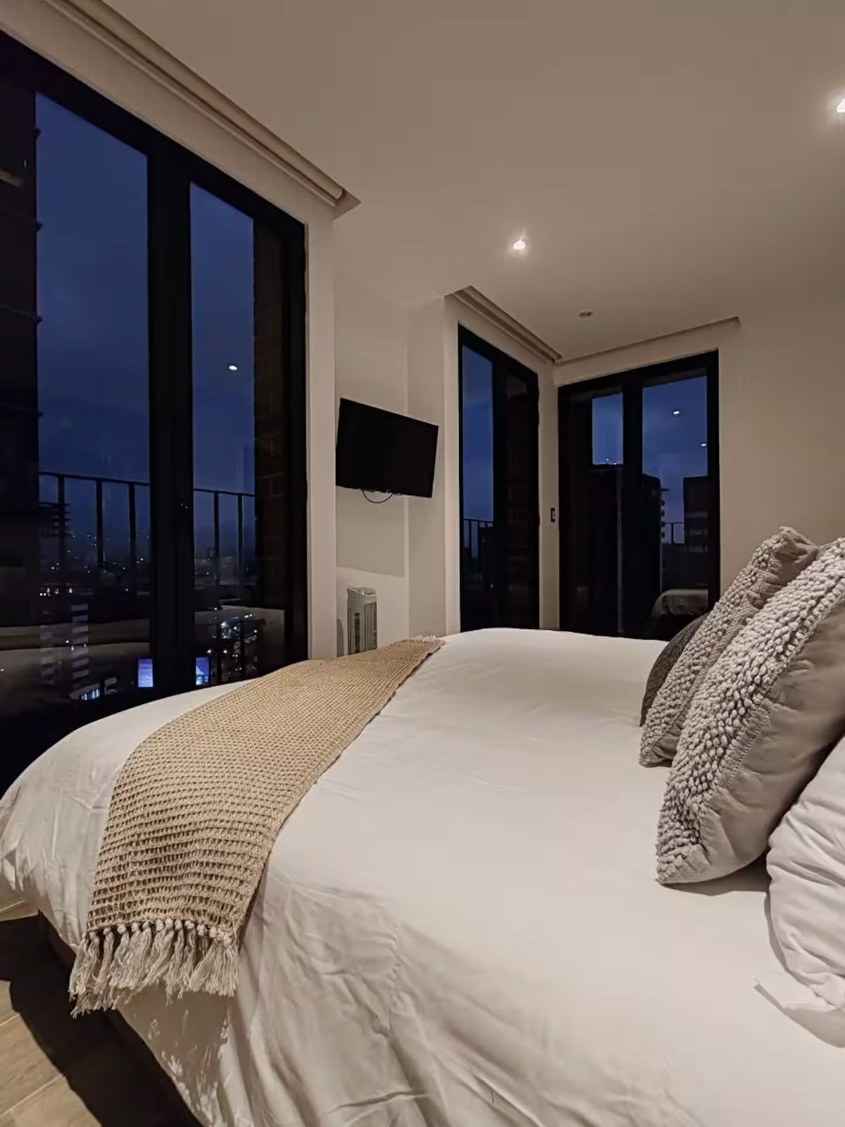 Une chambre avec un grand lit, une télévision et une vue sur le paysage urbain au crépuscule.