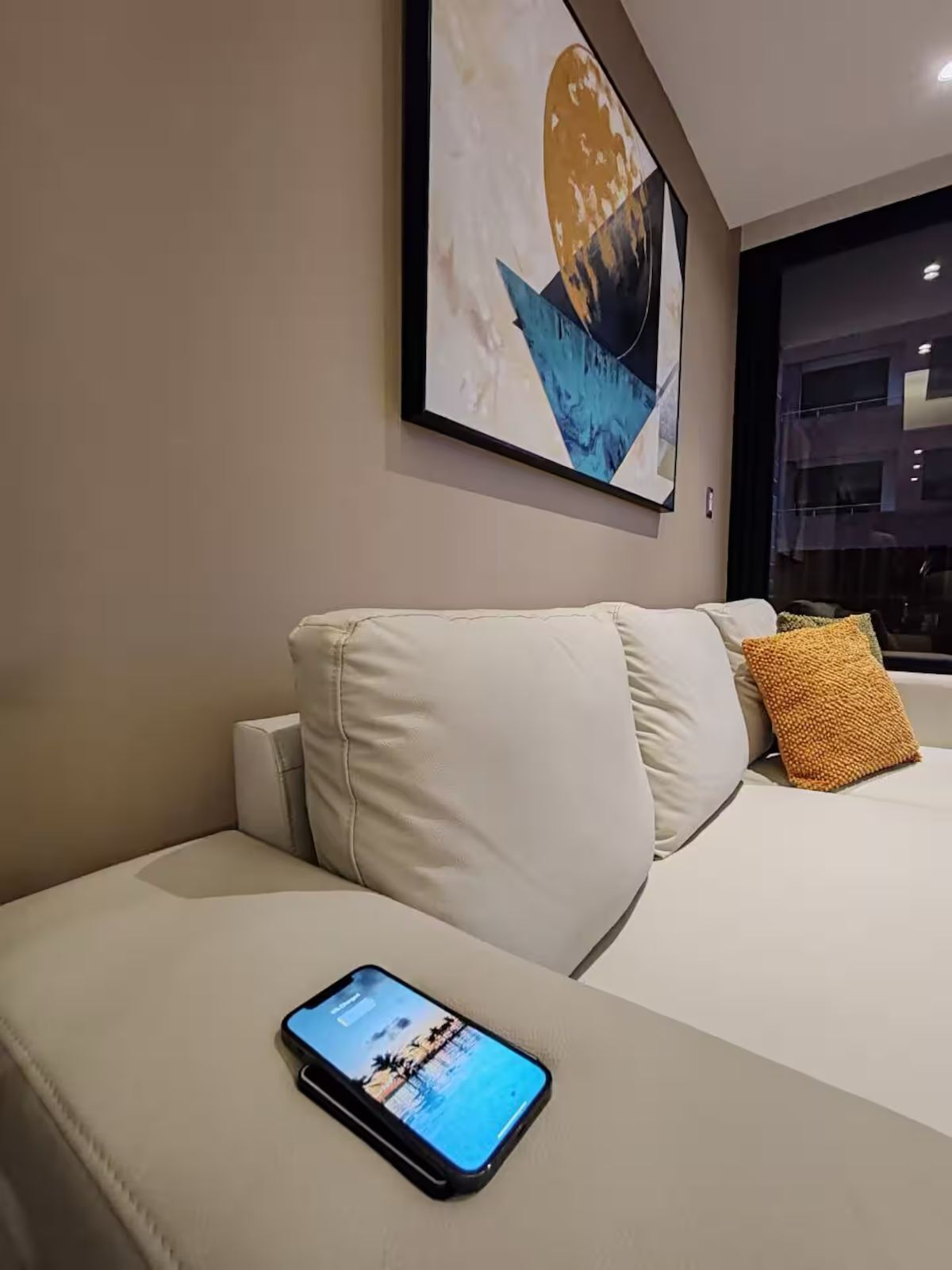 A modern hotel room with a white sofa, a smartphone on the armrest, and a large abstract painting on the wall.