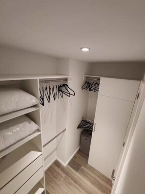 Ein begehbarer Kleiderschrank mit Regalen und Kleiderstangen, ein kleiner Stauraum sowie eine Tür zu einem weiteren Zimmer.