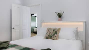 A hotel room with a bed, a door, a potted plant, and a view of another room.