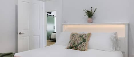 A hotel room with a bed, a door, a potted plant, and a view of another room.