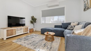 A modern living room with a flat-screen TV, a grey sofa, a wooden coffee table, and a patterned rug.