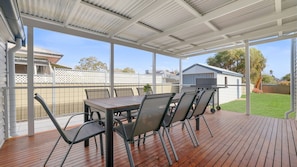 Une terrasse extérieure avec une table et des chaises, un barbecue et une vue sur une cour arrière clôturée.