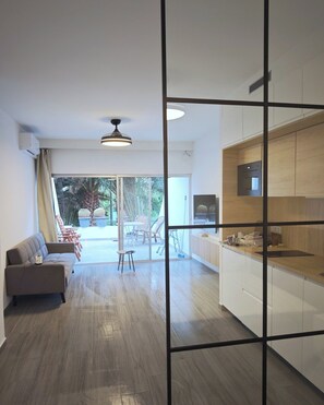 Une cuisine moderne avec des meubles blancs et un plan de travail en bois, un coin repas avec une table et des chaises, et un canapé.