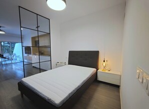 Un dormitori modern amb llit, taula de nit i una petita zona d'escriptori.
