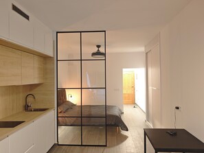 Una habitación funcional con kitchenette, una cama y una pequeña mesa.