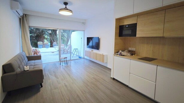 Uma sala de estar moderna com sofá, TV fixada na parede e porta de vidro deslizante para área externa.