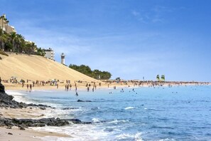 Una platja amb sorra, un far i una multitud de persones.