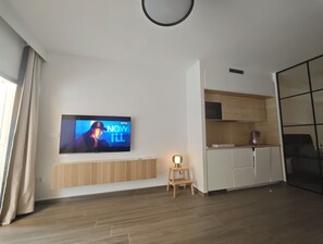 Una sala de estar moderna con un televisor de pantalla plana montado en la pared, armarios de madera, un taburete pequeño y un radiador debajo del televisor.