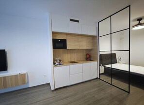 Habitació senzilla amb petita cuina, un llit i una finestra gran.