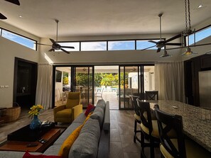 Un vaste espace de vie comprenant un grand canapé, une table à manger et des chaises, un ventilateur de plafond et une vue sur l’extérieur.