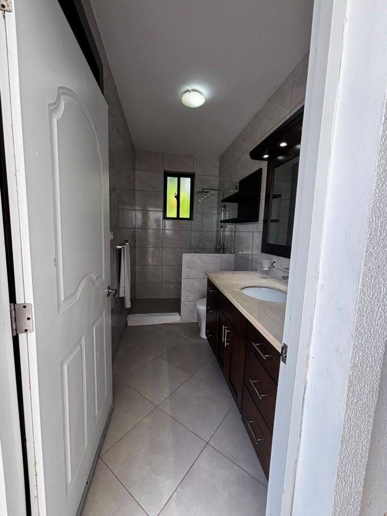 A bathroom with a white door, a shower, a sink, and a mirror.