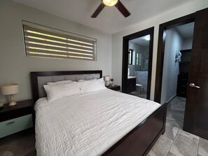 Une chambre à coucher avec un lit, des lampes de chevet, un ventilateur de plafond et une fenêtre avec des stores.