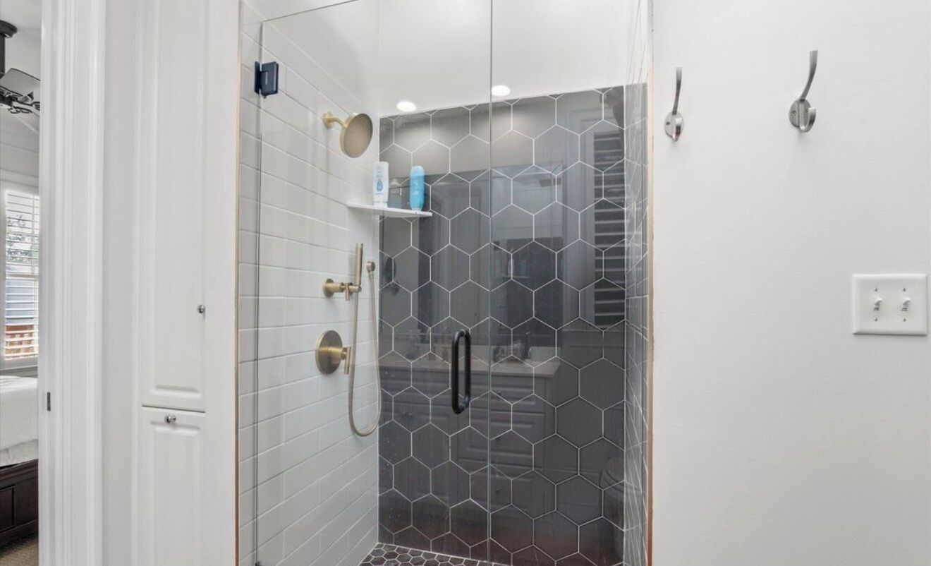 A bathroom with a glass-enclosed shower, white tiled walls, and a white door.