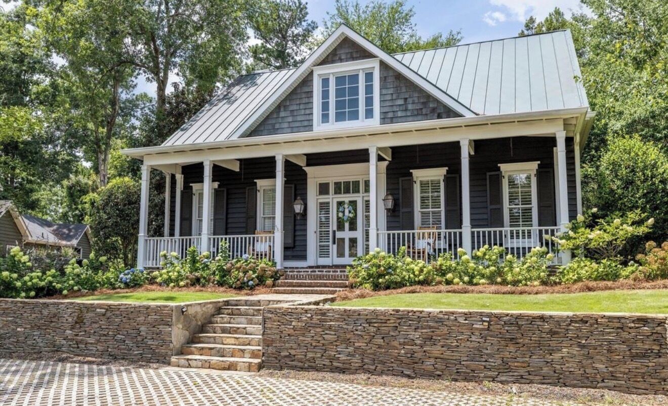 A two-story house with a covered porch, stone steps, and a stone wall.