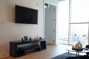 A modern living room with a flat-screen TV mounted on the wall, a dark console table with decorative items, and a large window offering a city view. - The Golden Hour Luxury Midtown Stay with Rooftop pool (Atlanta)