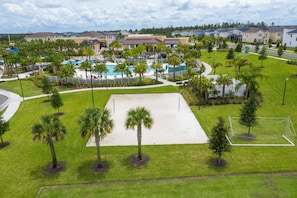 Un complex turístic amb zona de piscina, palmeres i un camp esportiu.