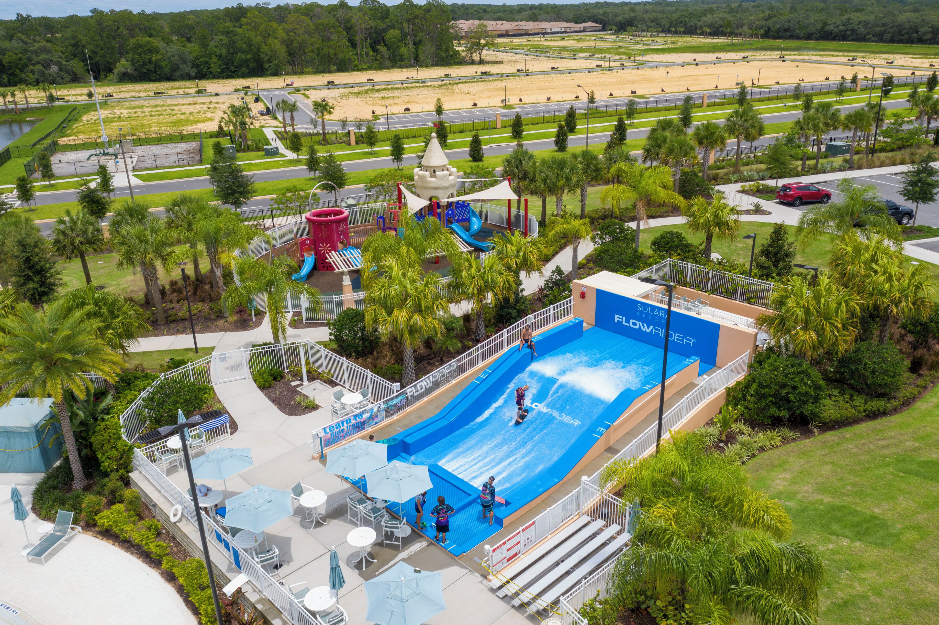 An aerial view of a water park with a large blue pool, slides, and palm trees.