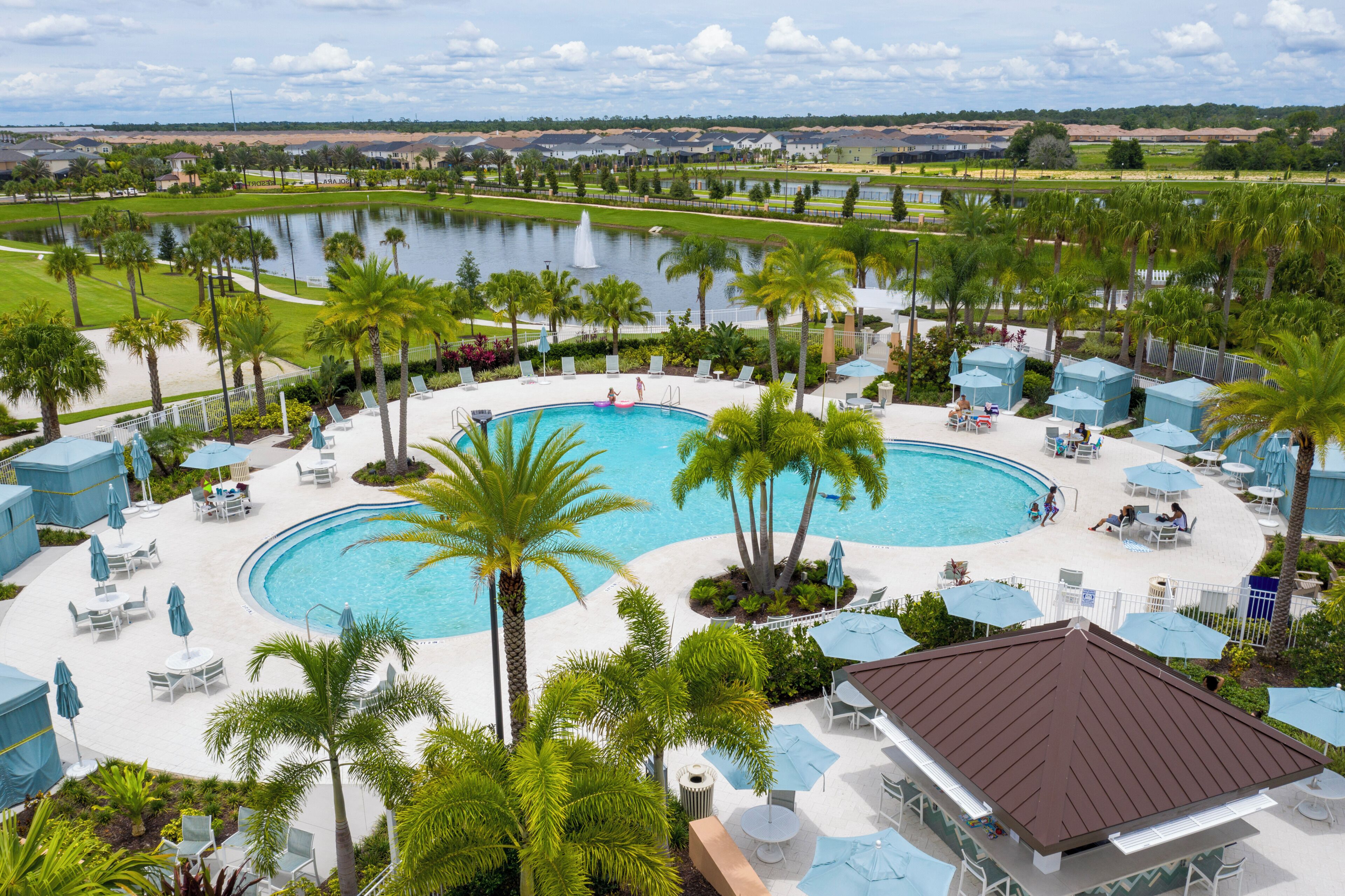 Een resort met een groot zwembad, palmbomen en uitzicht op een meer.