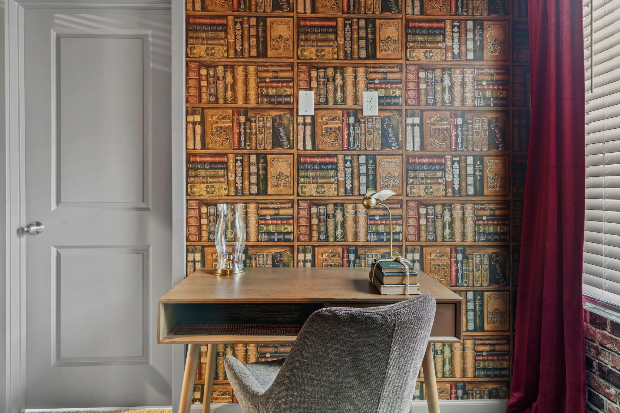 A room with a bookshelf filled with books, a desk with a lamp, and a chair.