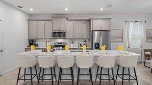 A modern kitchen with a central island, stainless steel appliances, and bar-style seating. - Brand New | 6BR Villa Pool & Spa,Loft near Disney 2380 (Kissimmee)
