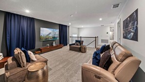 A modern living room with a flat-screen TV, comfortable seating, and a staircase leading to an upper level. - Brand New | 6BR Villa Pool & Spa,Loft near Disney 2380 (Kissimmee)