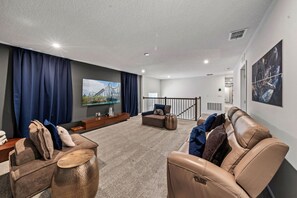 Ein modernes Wohnzimmer mit Flachbildfernseher, bequemen Sitzmöglichkeiten und einer Treppe zu einer oberen Ebene.