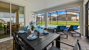 An outdoor patio with a table set for dining, a pool, and lounge chairs. - Brand New | 6BR Villa Pool & Spa,Loft near Disney 2380 (Kissimmee)