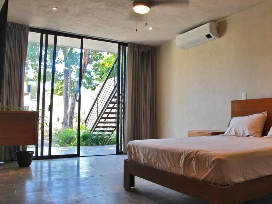 A bedroom with a bed, a nightstand, a potted plant, and a sliding glass door leading to an outdoor area.
