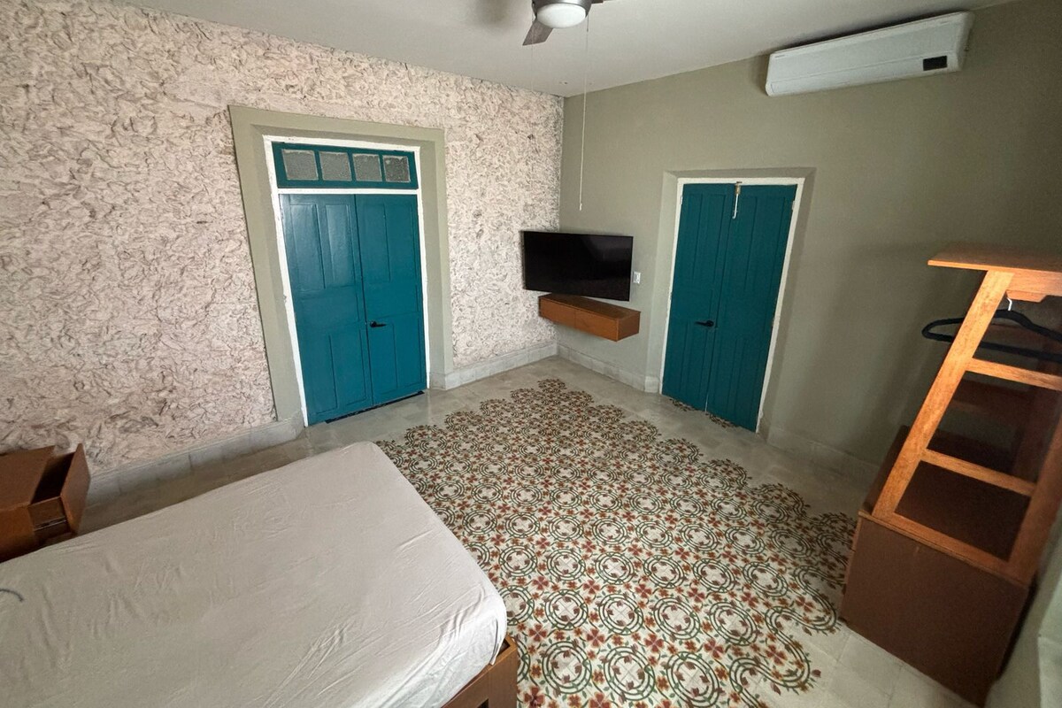 A bedroom with a bed, a ceiling fan, a TV mounted on the wall, and two doors.
