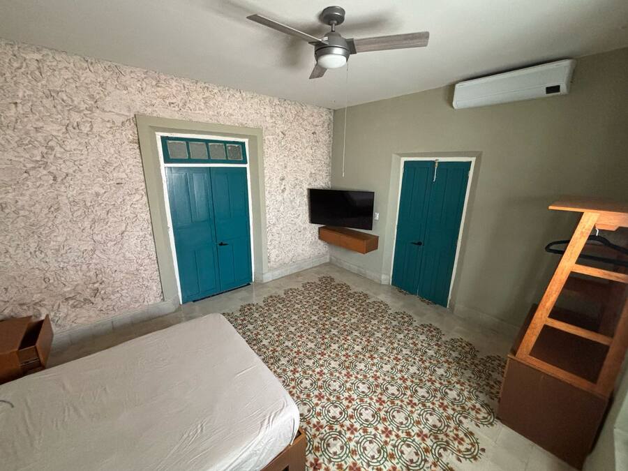 Un dormitorio con cama, ventilador de techo, televisor montado en la pared y dos puertas.